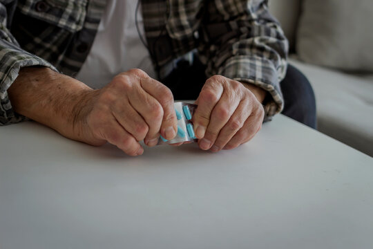 Photo of a senior man's hands taking pills and medications. Unhealthy middle aged old man holding a pill unpacks tablets before use. Healthcare, medicine, pharmacy and elderly concept. Close up.