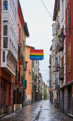 Fototapeta na wymiar Gay pride flag waving on a rainy day, through old streets of the Vitoria-Gasteiz, Basque country 