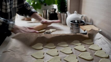 Close up of a heart cookie on a baking sheet. The girl prepares cookies, rolls out the dough with a wooden rolling pin, cuts out the heart. Surprise for Valentine's Day, Mother's Day, Father's Day