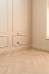 Close up view of modern and bright interior of empty cream colored room corner with herringbone parquet floor