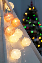 teepee tent with illuminated light bulb garland in nursery room at christmas holidays with christmas tree