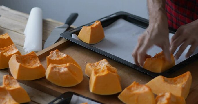 Sweet pumpkin pieces put onto baking tray with baking paper sheet prior roasting, close up, obscured face