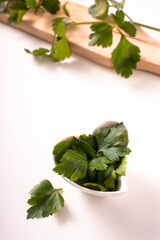 heart-shaped bowl with parsley leaves, near cutting board with parsley sprigs on top. White background. love concept for parsley. aromatic herb.