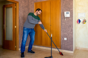 Bearded man sweeping the ceramic floor of his house. Selective focus