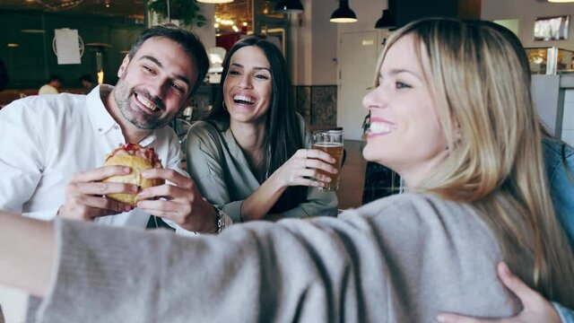 Video of happy group of friends taking selfie with smart phone while eating burgers in a restaurant.