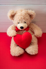 Valentines day. Teddy bear holding a red heart sitting on red floor