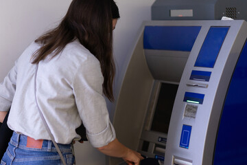 Young woman uses ATM to withdraw cash or pay for services, public place