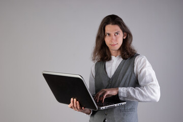 Training and new technologies, online courses, e-learning. A young man with long hair and glasses. A student is holding a laptop