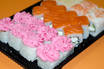  set of sushi in  black disposable box on an orange background. Rice rolls with fish and caviar, Japanese cuisine.