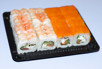 Japanese cuisine.  set of sushi in  black disposable box on  blue and white background. Rice rolls with shrimp and flying fish roe.
