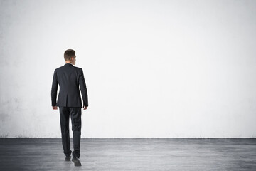 Rear view of young businessman walking forward in empty concrete room