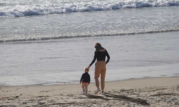 Mulher a passear uma crian&ccedil;a na areia da praia perto do mar ao fim da tarde, m&atilde;e a passear filho