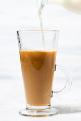 milk is poured into a glass cup with coffee, vertical