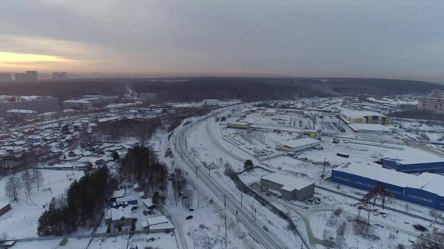 Aerial view of Industrial Zone at Outskirts of the city at evening. There are many one-story private houses and several multi-story buildings. Near the railway and forest. Winter evening.
