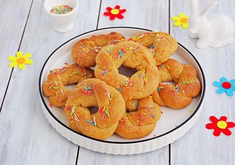 Traditional buttery twisted Italian Easter cookies with multicolored sugar decor on a white plate on a white wooden background. Easter sweets.