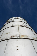 Vertical view of a Silo made of metal silver colored panels close-up with bright blue sky in the background.