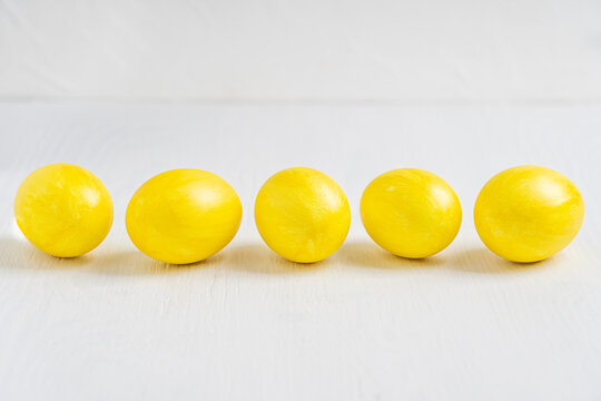Side view of five painted in bright yellow color boiled eggs prepared for easter celebration party laying on white wooden background in a line at the center. Image with copy space, horizontal