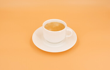 White cup with coffee on orange background