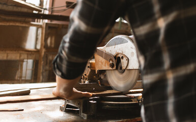 Close-up of a carpenter using a chop saw to cut wood plank.