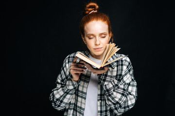 Portrait of charming young woman college student standing with closed eyes holding opened book on...