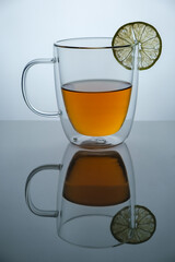 Glass cup with hot tea and lemon on mirror surface, studio advertising shot, copy space