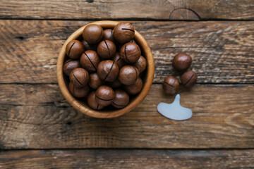 Bowl with whole tasty organic macadamia nuts on wooden background. Metal key for macadamia nut. Macadamia integrifolia in shell. Healhty snack. Top view. Soft focus