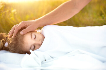 Girl sleeps on white bed in the grass, fresh air. Dad's hand gently pats his head. Eco-friendly lifestyle, healthy sleep, benefits of ventilation, hardening, clean nature, ecology, children's health