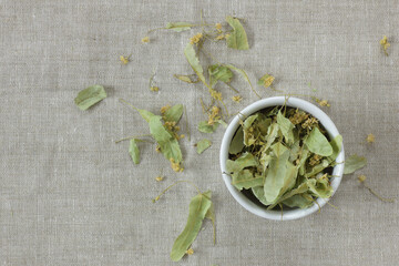 Dried lime-blossoms from above on linen textile with lime leaf flower buds neaby, overhead top view, flat lay, closeup, copy space, herbal tea nad naturopathy concept