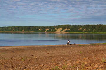 A beautiful panorama of a lake with a flat rocky beach and a steep coast with a forest on the other side and a couple of tourists woman and man near the water on a summer sunny day.Travel concept