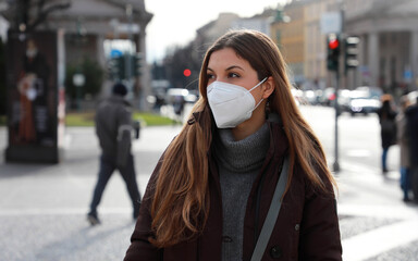 Sense of bewilderment. Young woman in winter clothes walking in street wearing protective mask FFP2...