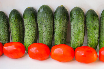 Several green cucumbers and red tomatoes are stay in a rows on a white background