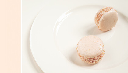 Obraz premium Two light delicious french macaroons on a light plate, trend color 2021 Set Sail Champagne, minimalist composition close-up
