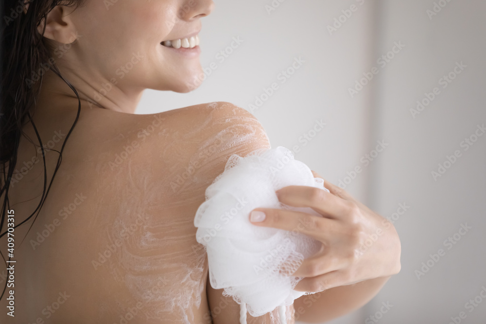 Wall mural crop close up of smiling young caucasian woman take shower rub massage body with foam gel using puff