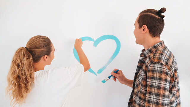 Young couple drawing heart on the wall. Family having fun during painting the wall blue in a new apartment. Do it yourself and Happy Valentines day concept