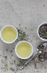 Thyme dried flower herbal tea in a white chinese cups on linen textile with blossoms and spoon nearby, closeup, copy space, flat lay, from above overhead top view, healthy herbal teas  concept