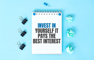 White notepad with text Invest in Yourself It pays the best interest and office tools on the blue background