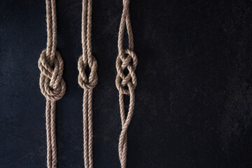Flat lay set of three nautical knots tied on natural ropes. Ropes are parallel on a dark background