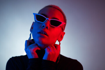 Portrait of a young woman with a short male haircut in sunglasses in neon light in the studio