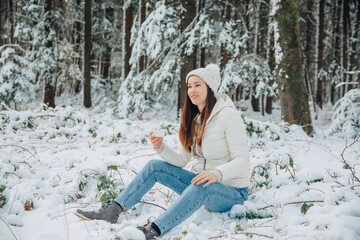 woman sitting on the snow. Woman in the forest has tea in her hands. Woman sitting in forest, drinking tea	