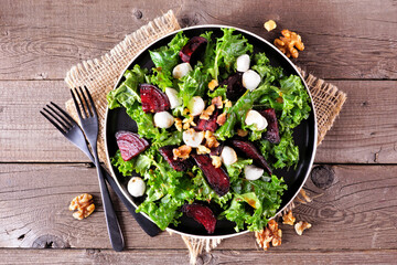 Healthy kale and beet salad with cheese and walnuts. Above view table scene over a rustic wood...