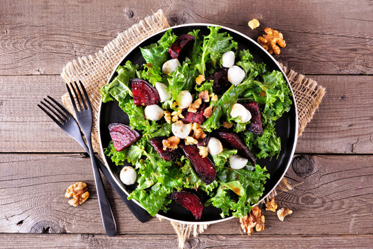 Healthy kale and beet salad with cheese and walnuts. Above view table scene over a rustic wood background.