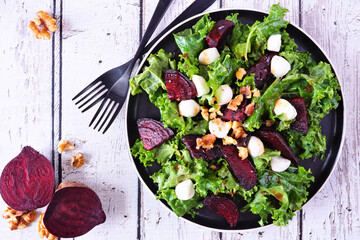 Healthy kale and beet salad with cheese and walnuts. Top view table scene over a white wood...