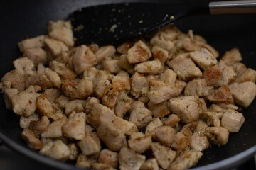 Cooking chicken cubes in a black frying pan