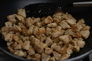 Cooking chicken cubes in a black frying pan