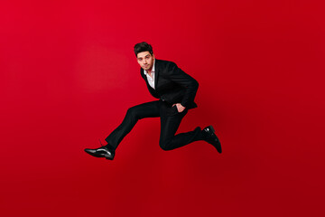 Fototapeta na wymiar Good-looking man in stylish suit jumping on red background. Studio shot of brunette guy having fun.