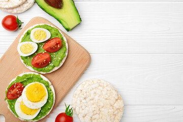 Top view rice cakes with avocado mash and eggs with tomato on wooden background with copy space