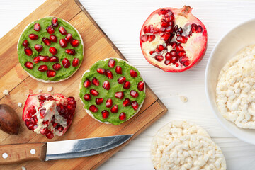 Top view rice cakes with avocado mash and pomegranate seeds on cutting board