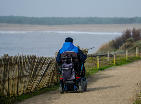 Vendée, France; January 29, 2021: A Disabled Person In An Electric Wheelchair On The Protected Hiking Trail That Runs Along The Corniche Of Saint Hillaire De Riez.