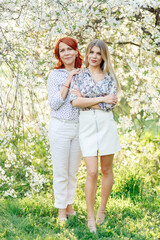 Fototapeta premium Two women, one young and the other older, in the spring in a beautiful garden with white flowers. Full-length photo