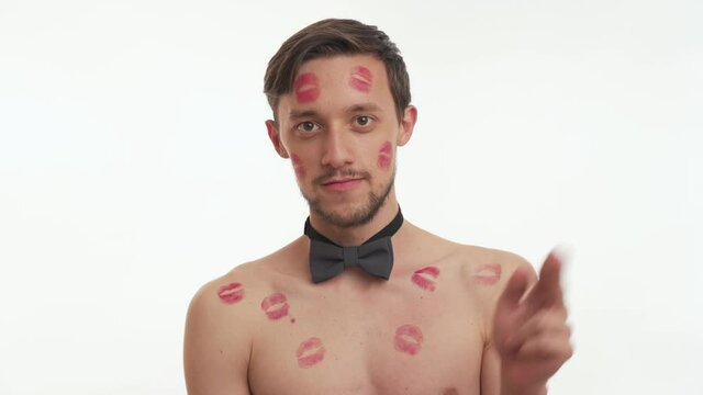 One lovely Caucasian man with short brown hair, kissed by girlfriend with lipstick kiss marks on face and body blow kisses from the fingers of his hands isolated on white background. Romantic concept.